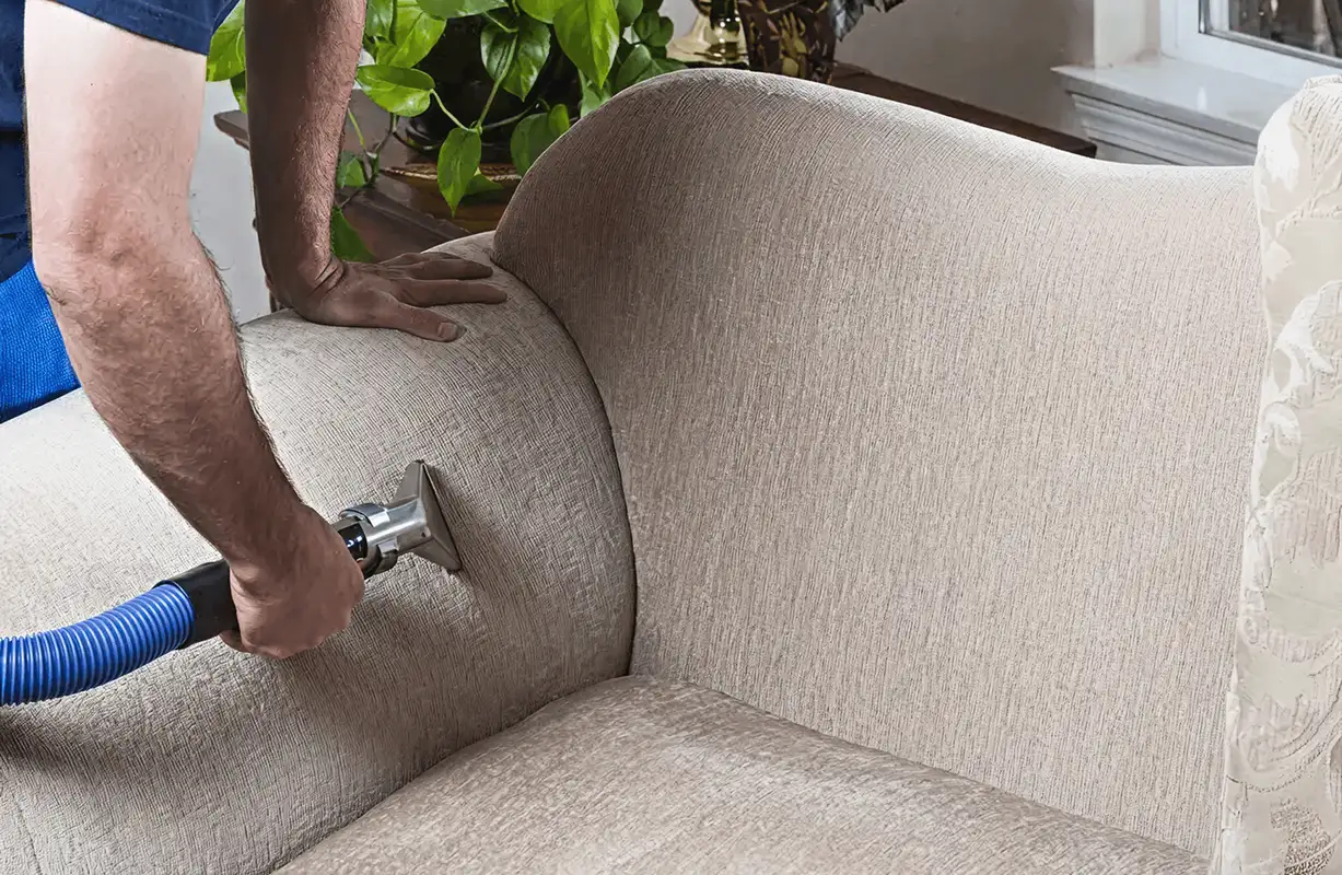Professional upholstery cleaner deep-cleaning a fabric sofa with a handheld extraction tool and hose, Green Bay, WI.